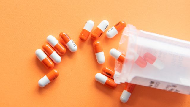 Orange and white capsules spilling from a plastic bottle. 