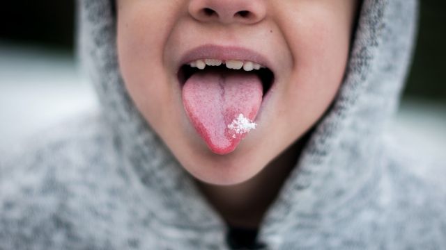 A child poking out their tongue catching a snowflake on it. 