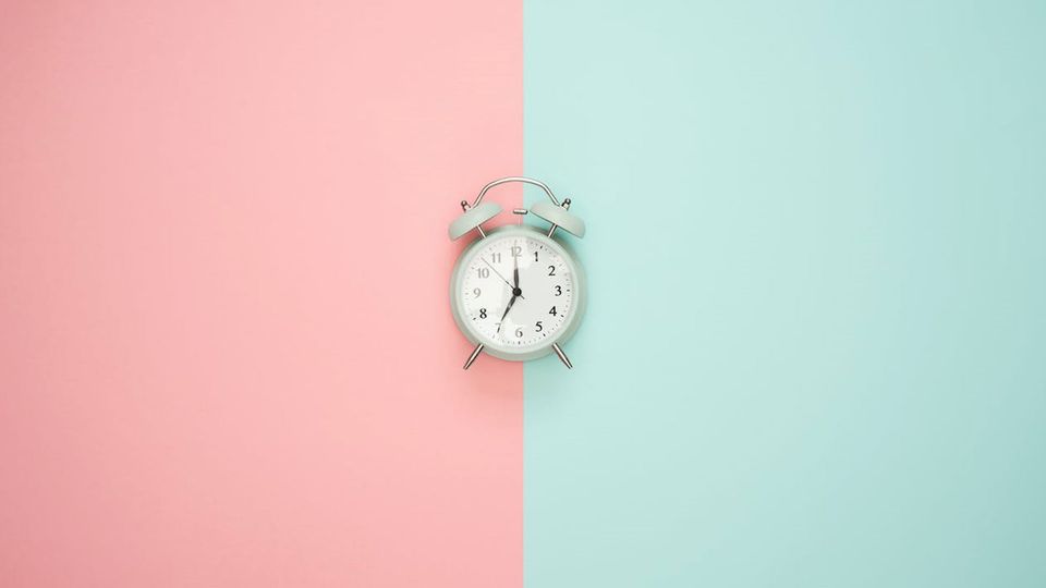 A clock on a pink and blue split background.