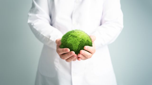 Scientist in a lab coat holding a green model of the Earth. 