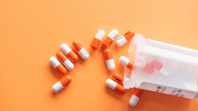 Orange and whit pill capsules spill from a clear bottle. 