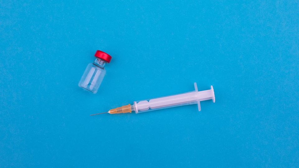 A syringe and a vaccine vial on a blue background.