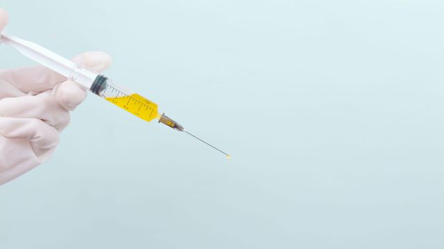 A gloved hand holds a syringe filled with yellow liquid. 